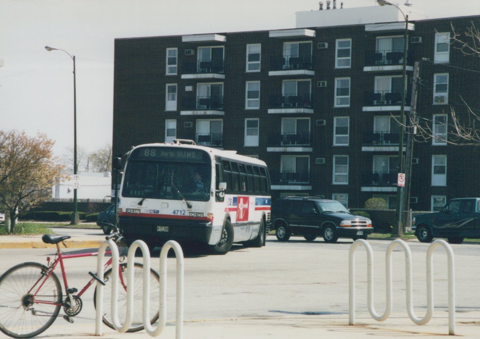 A white and red CTA bus, number 4712, on route 88, parked on a street with a red bicycle locked to a rack in front and a black apartment building in the background.