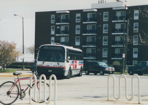 A white and red CTA bus, number 4712, on route 88, parked on a street with a red bicycle locked to a rack in front and a black apartment building in the background.