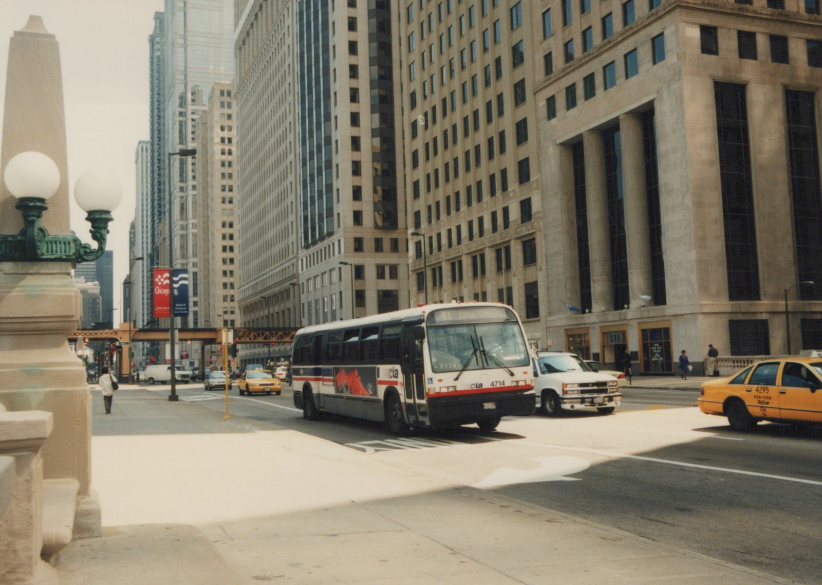 A Chicago Transit Authority bus, number 4714, is driving on a city street with tall buildings behind it; a yellow taxi and other vehicles are nearby.