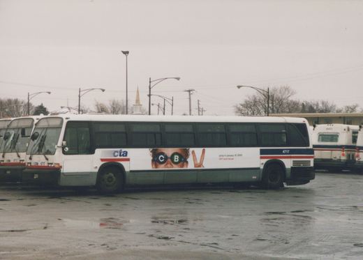 Side view of a white Chicago Transit Authority bus number 4717 parked in a wet lot, with a 'jump in january 15 2000' ad on its side, and other buses nearby under an overcast sky.