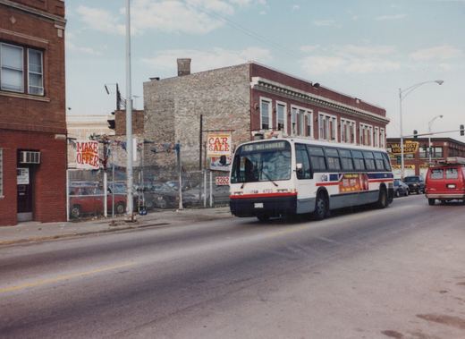 A white, blue, and red Chicago Transit Authority bus, number 4723, is driving down a city street with commercial buildings and signs in the background.