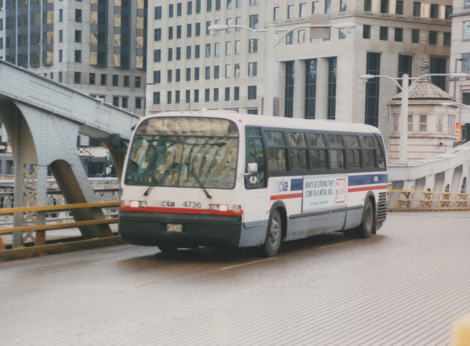 A white and blue CTA bus with route 41 Elston/Clybourn written on its front is driving across a steel bridge in a city with tall buildings in the background.