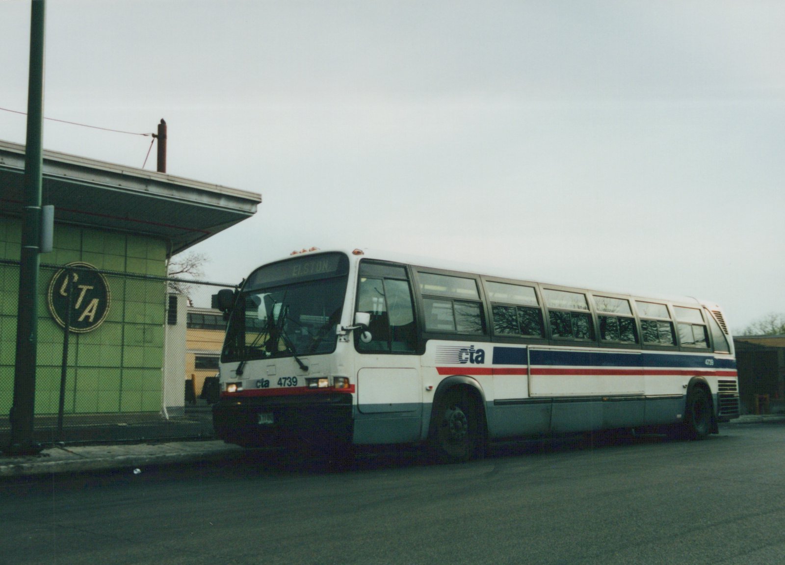 A white, blue, and red Chicago Transit Authority bus, numbered 4739, is parked on a street next to a green tiled building with a CTA sign.