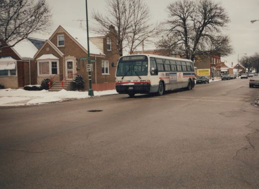 A white Chicago Transit Authority bus with blue and red stripes, numbered 4741, is turning a corner on a snow-lined residential street, with brick houses and bare trees in the background.