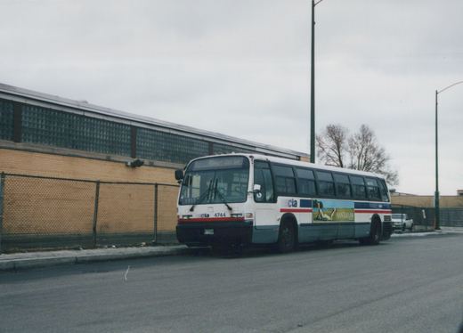 A white, red, and blue Chicago Transit Authority bus, number 4744, is parked on a street next to a brick building with a chain-link fence.