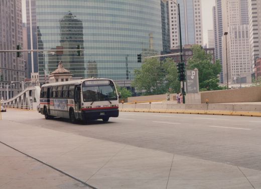 A white and blue Chicago Transit Authority bus, route 41 to Clybourn, drives on a city street with a large glass skyscraper behind it.