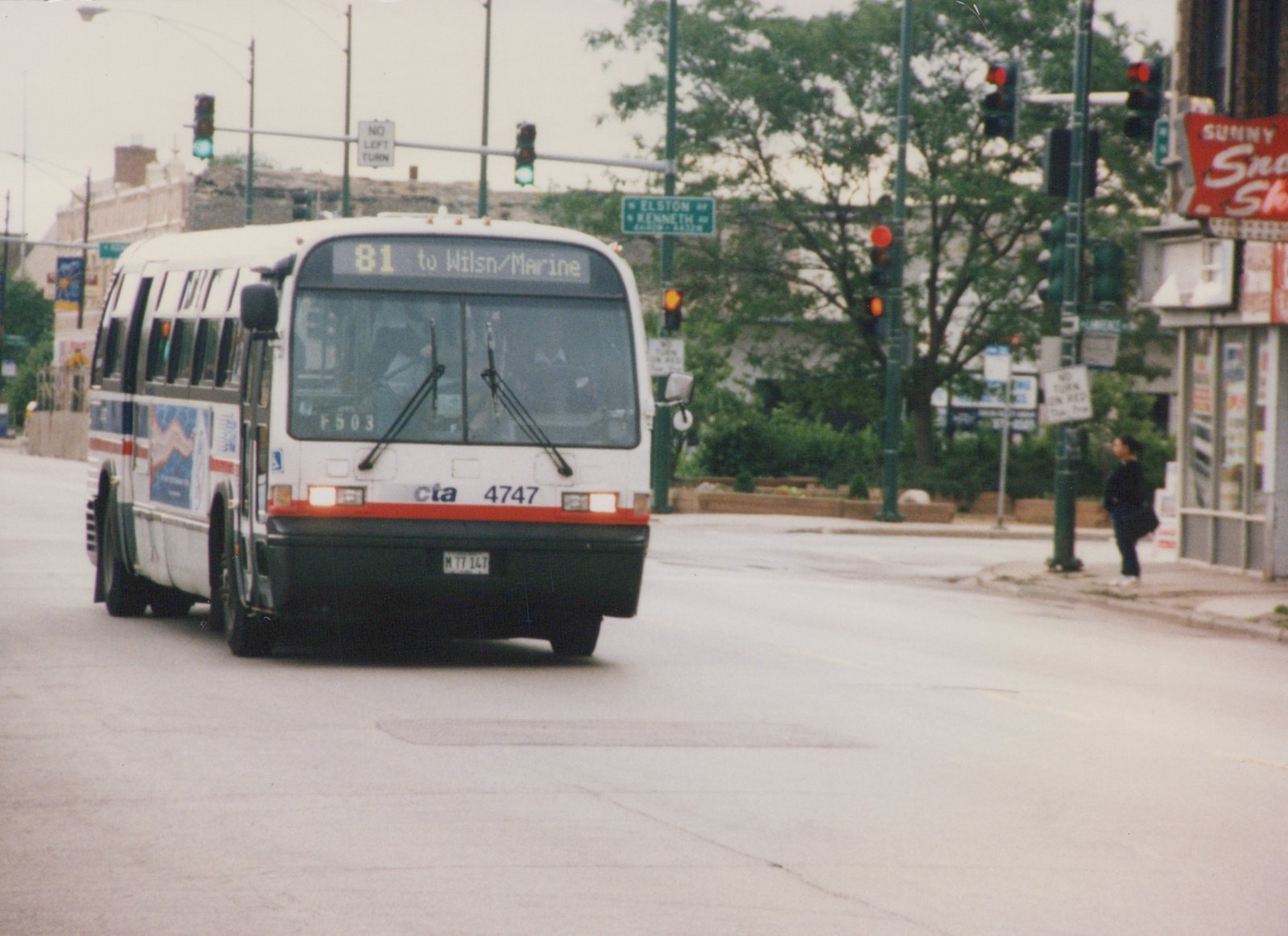 A white and red Chicago Transit Authority bus, number 4747, is shown at an intersection with traffic lights and street signs, with a person visible on the sidewalk.