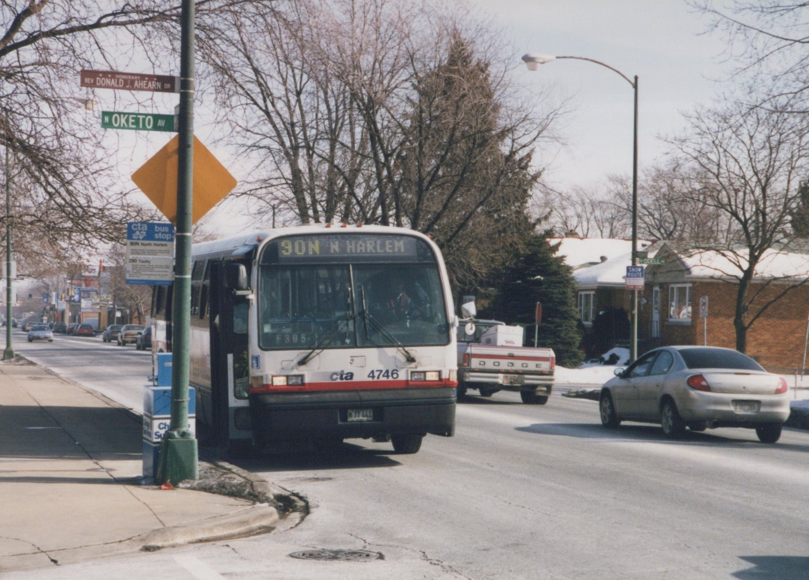A white and red Chicago Transit Authority bus, number 4746, is stopped at a bus stop on a snowy street, with the destination '90N N Harlem' displayed; bare trees and a clear sky are in the background.