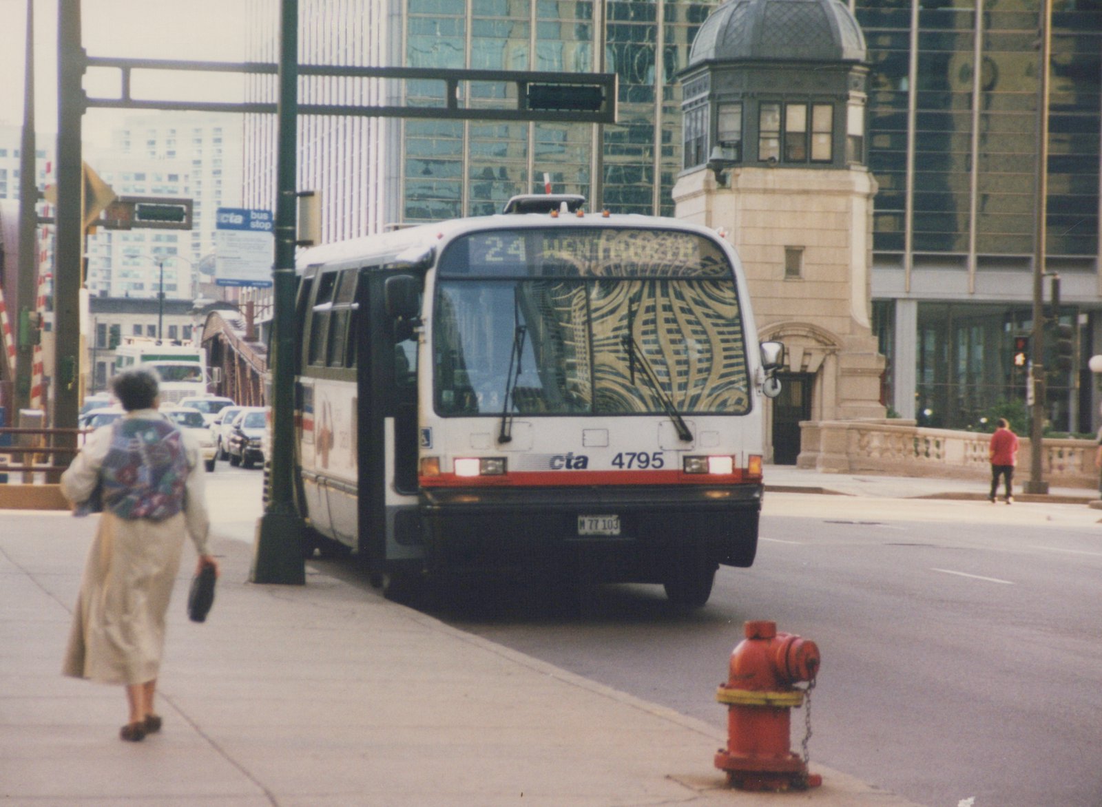 Front three-quarter view of a white and red CTA bus number 4795 with '24 WENTWORTH' on its destination sign, stopped at a city street corner with pedestrians nearby.