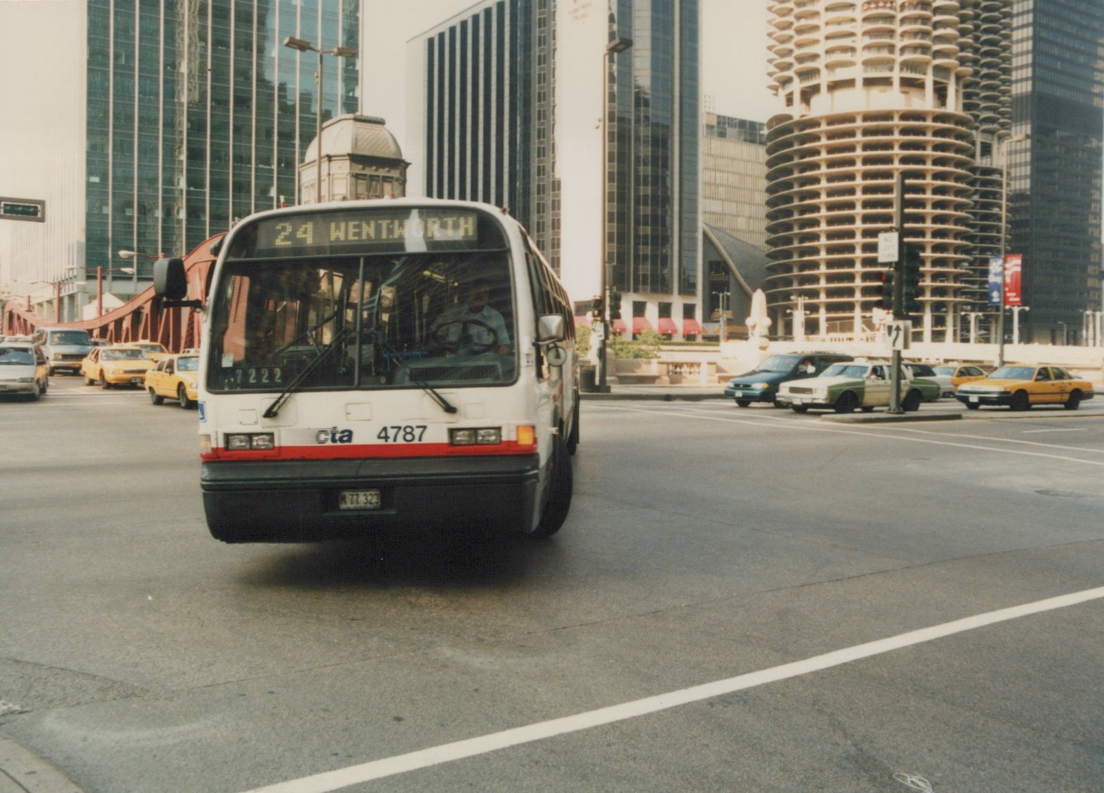 A white Chicago Transit Authority bus, number 4787, is shown head-on, driving down a city street lined with tall buildings and other vehicles.