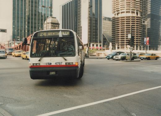 A white Chicago Transit Authority bus, number 4787, is shown head-on, driving down a city street lined with tall buildings and other vehicles.