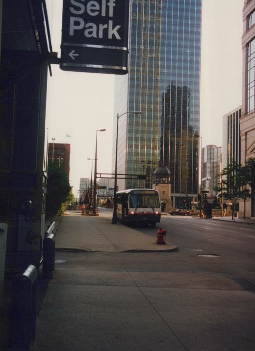 A white and red Chicago Transit Authority bus, number 4795 on route 24, is seen from a low angle on a city street with tall buildings in the background, under an overcast sky.