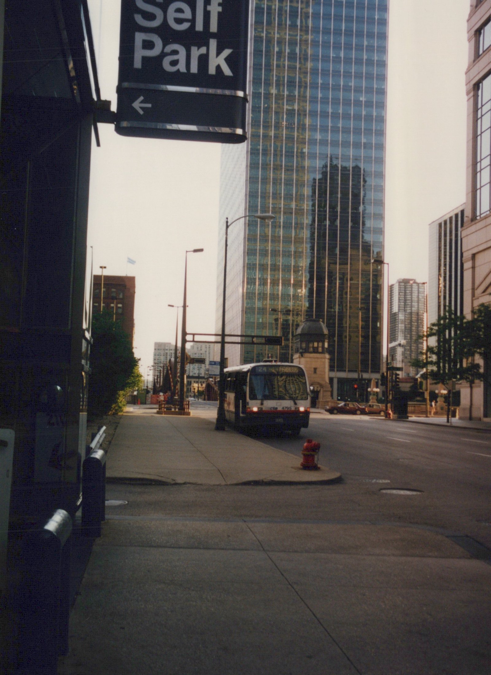 A white and red Chicago Transit Authority bus, number 4795 on route 24, is seen from a low angle on a city street with tall buildings in the background, under an overcast sky.