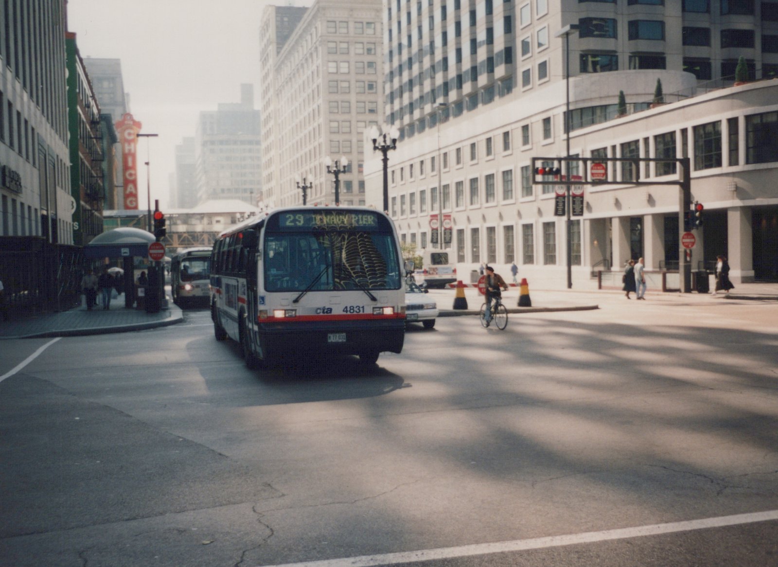 Front view of a white Chicago Transit Authority bus with red and blue stripes, numbered 4831, driving on a city street with pedestrians and another bus in the background.