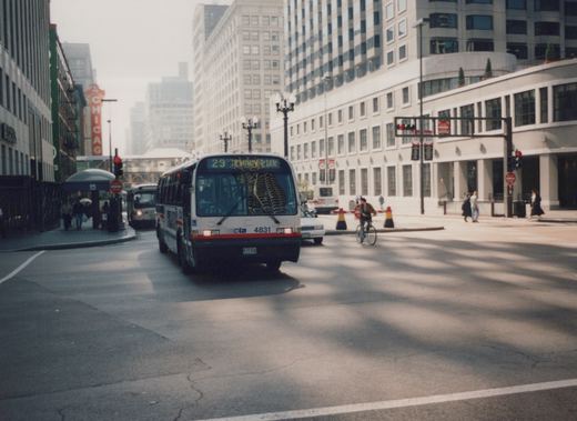 Front view of a white Chicago Transit Authority bus with red and blue stripes, numbered 4831, driving on a city street with pedestrians and another bus in the background.