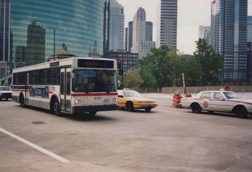 A white CTA bus with the number 4131 on the front drives down a street in Chicago, surrounded by other vehicles and tall glass buildings in the background.