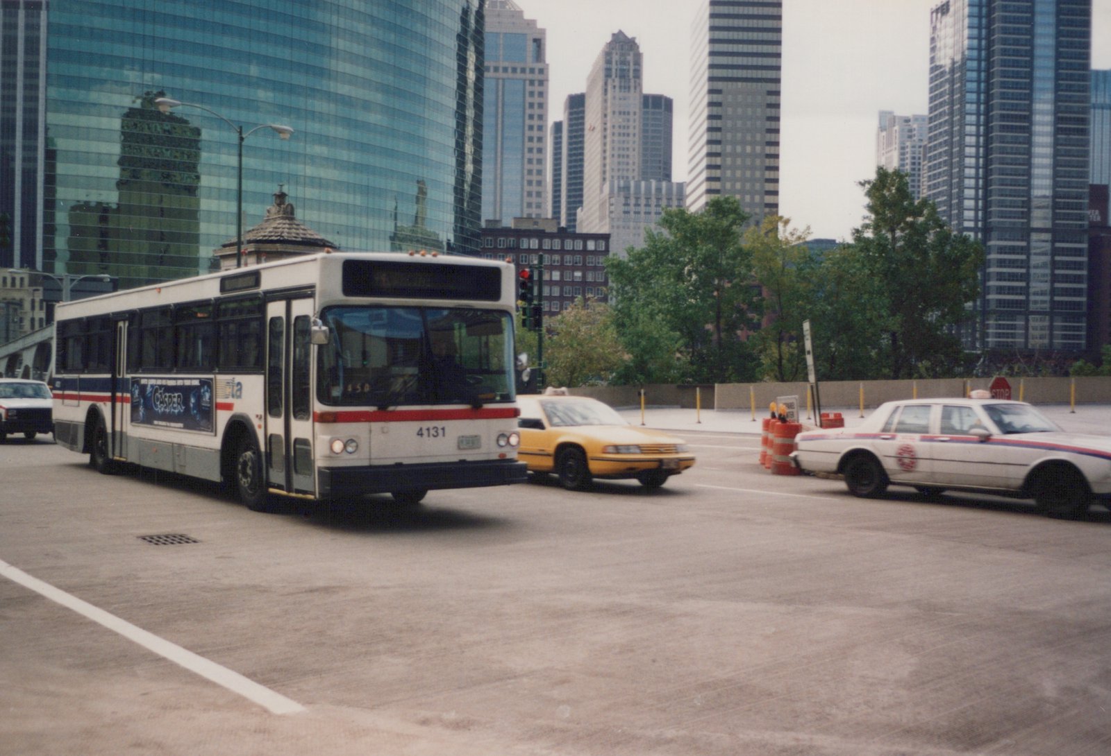 A white CTA bus with the number 4131 on the front drives down a street in Chicago, surrounded by other vehicles and tall glass buildings in the background.
