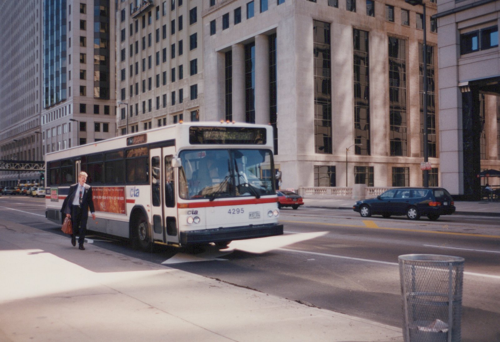 A white and red CTA bus numbered 4295 with a destination sign reading 'WACKER + FRANKLIN' is stopped on a city street, with a man in a suit walking past it.