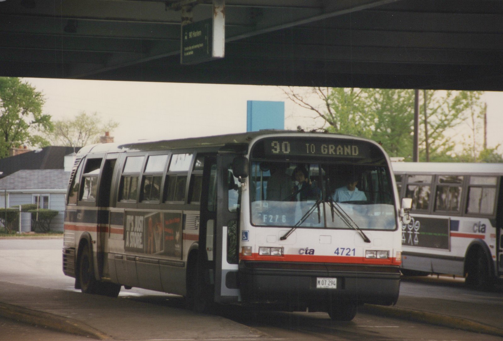A white and gray Chicago Transit Authority bus with the number 4721 on the front, displaying route 90 to Grand, is stopped under a bridge at a bus terminal, with another CTA bus visible behind it.