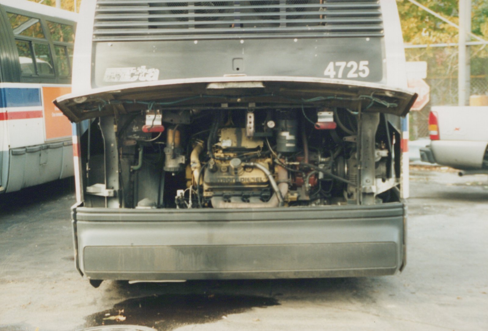Rear view of a white Chicago Transit Authority bus with its engine compartment open, showing a Detroit Diesel engine, parked in a lot with other vehicles nearby.