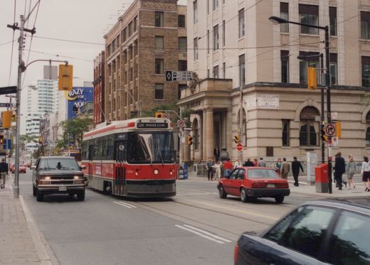 A red and white streetcar signed 504 Broadview Station comes toward the camera on a city street beside a dark pickup truck, with stone office buildings and pedestrians on the right.