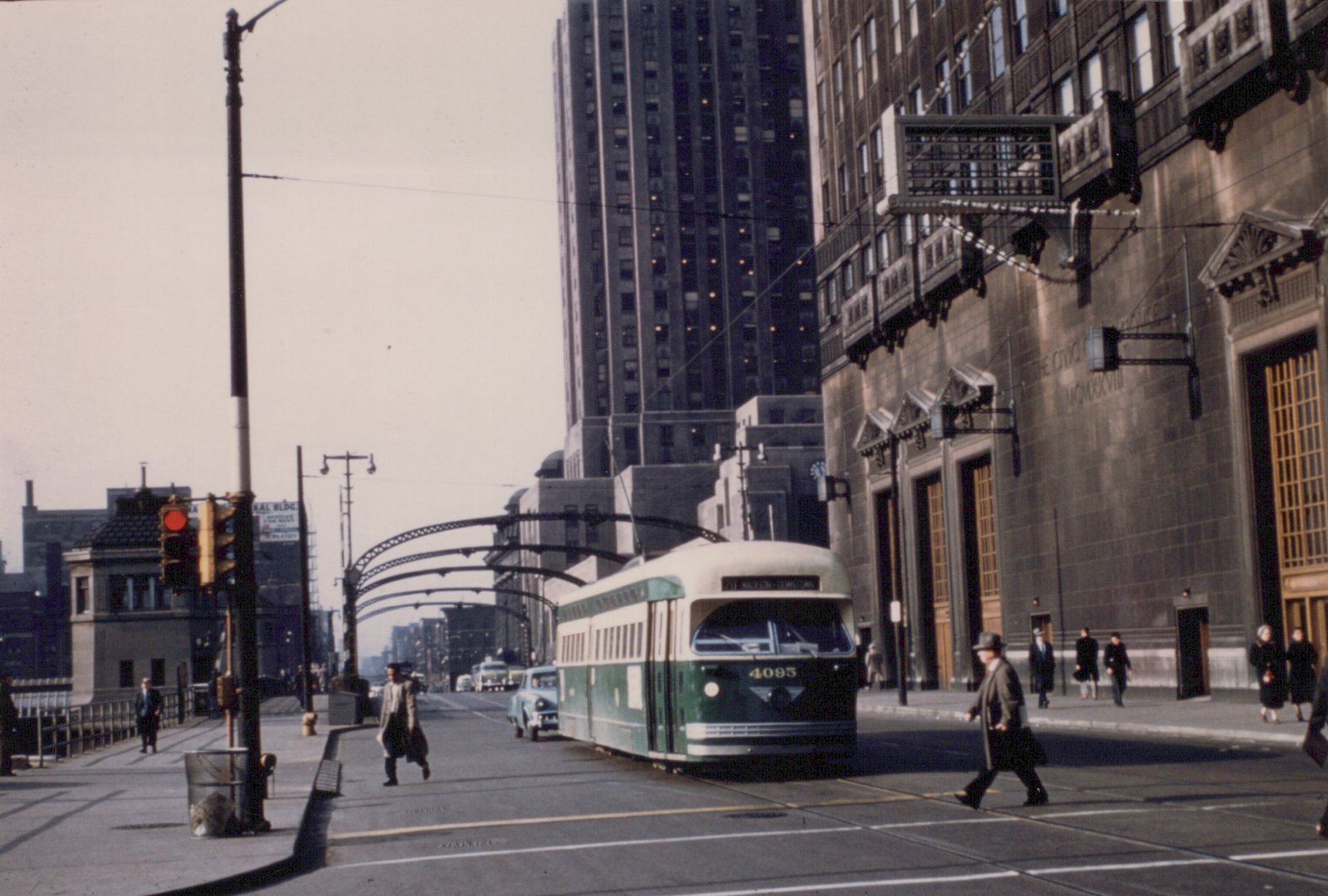 A green and cream PCC streetcar numbered 4095 on a city street with pedestrians crossing, tall buildings in the background, and overhead trolley wires.