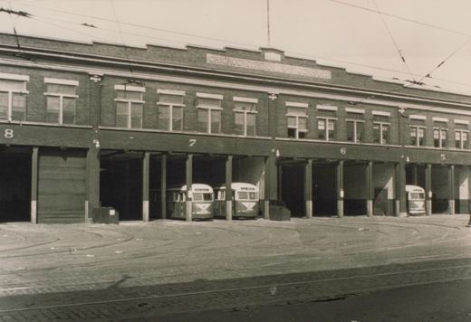 A two-story brick carbarn lettered Chicago City Railway Company with numbered open bays. Three streamlined streetcars are parked inside, with curving tracks and overhead wires in front.