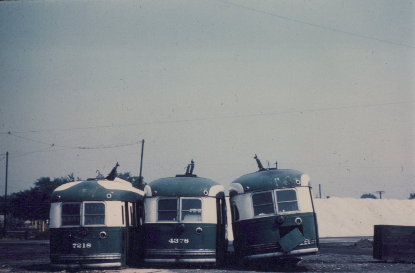 Three green and cream PCC streetcars, numbered 7218, 4378, and 2218, are parked nose-to-nose in a yard under an overcast sky, with overhead wires visible above.