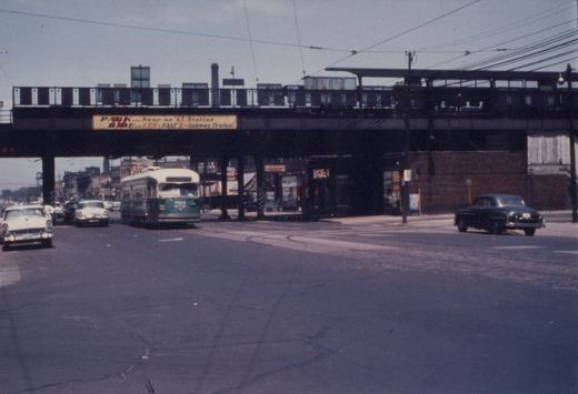 A green and cream streetcar comes toward the camera on a wide street, under a steel elevated railway bridge that carries a CTA 'Park and Ride' sign, with 1950s cars on both sides.