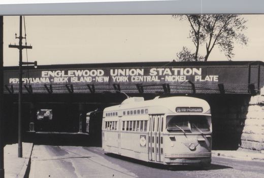 Black-and-white photo of a streamlined streetcar with a single trolley pole, signed 36 119-MORGAN, coming out from beneath a riveted steel railroad bridge lettered ENGLEWOOD UNION STATION.