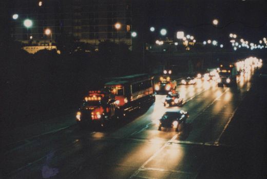 A blurry nighttime photo of a multi-lane highway in Chicago, with a red-fronted bus and several cars, lights streaking across the dark scene.