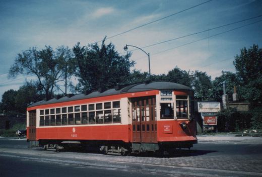 A vintage red and cream streetcar, number 6205, marked with route 93-95, stands on a tree-lined street under an overcast sky, with a Coca-Cola sign visible in the background.