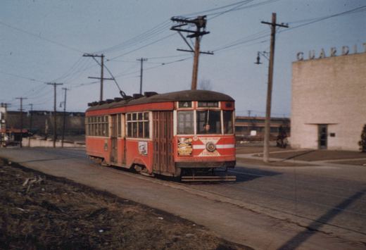 A vintage red and cream streetcar with the number 6296 and route 4 sign is moving down a street with overhead wires and a building labeled 'GUARDIT' in the background.
