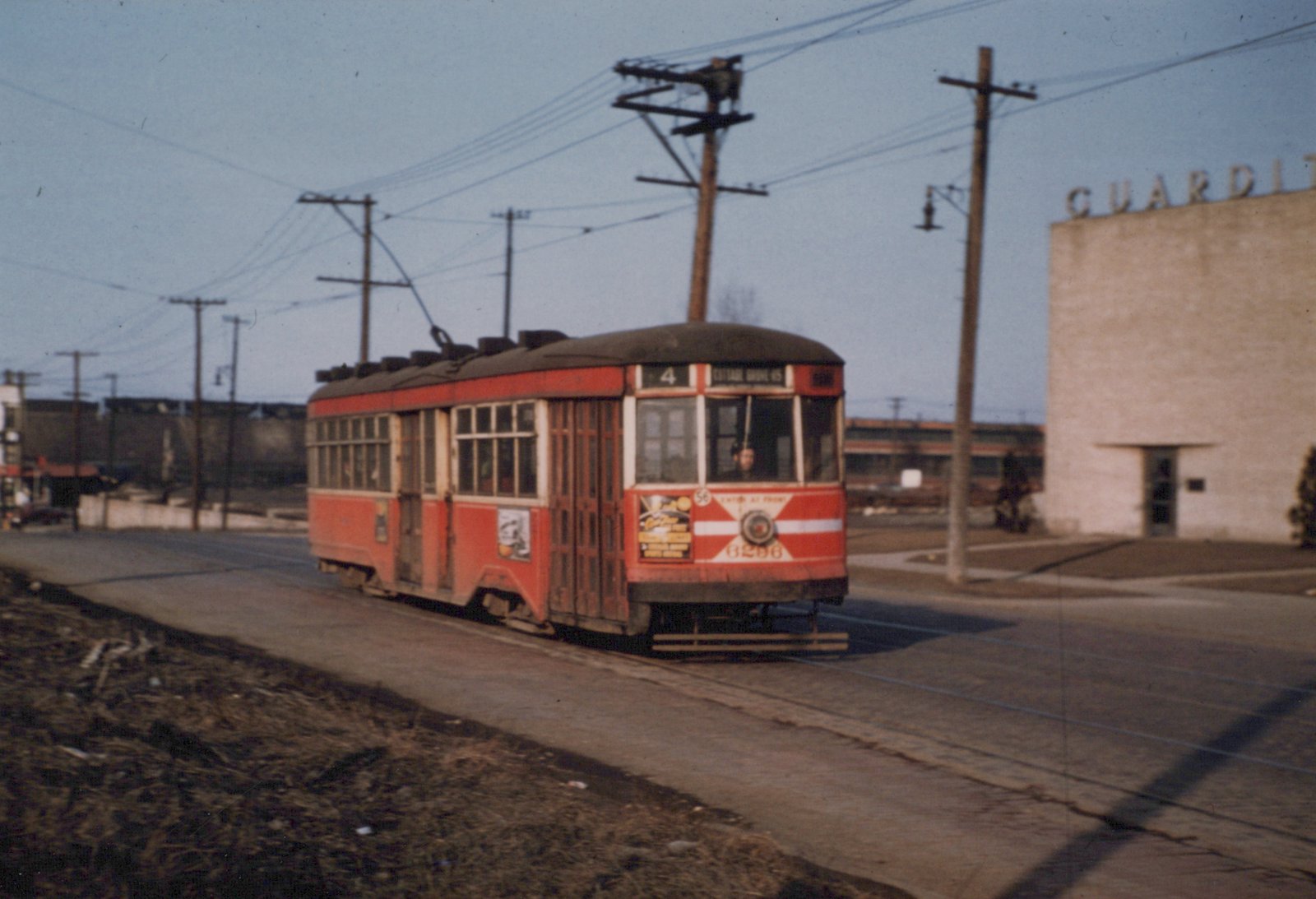 A vintage red and cream streetcar with the number 6296 and route 4 sign is moving down a street with overhead wires and a building labeled 'GUARDIT' in the background.