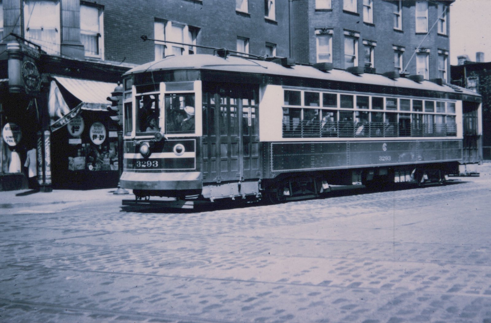 A vintage black and white photo of Chicago Surface Lines streetcar 3293, a Master Unit, stopped on a cobblestone street with storefronts in the background.