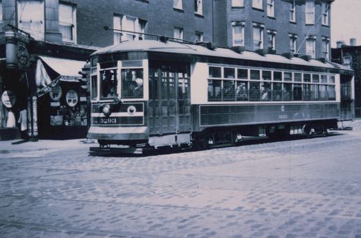 A vintage black and white photo of Chicago Surface Lines streetcar 3293, a Master Unit, stopped on a cobblestone street with storefronts in the background.