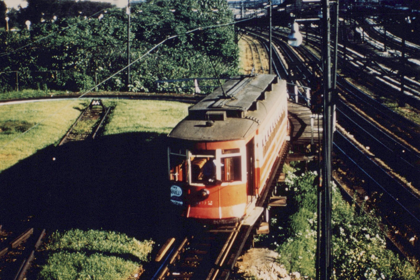 A red and cream interurban car numbered 396 travels on an elevated wooden trestle, surrounded by greenery with a network of tracks in the background.