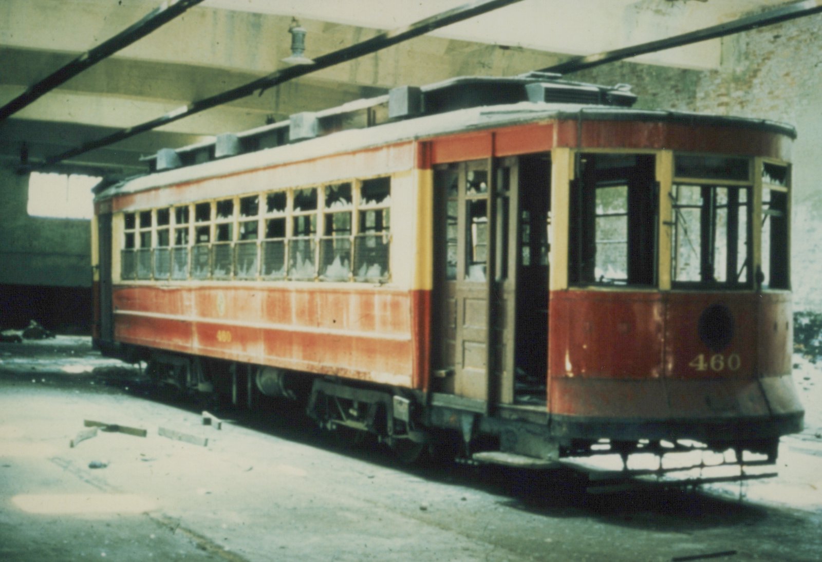 A red and cream streetcar with broken windows, number 460, is parked under a concrete bridge in a state of disrepair.