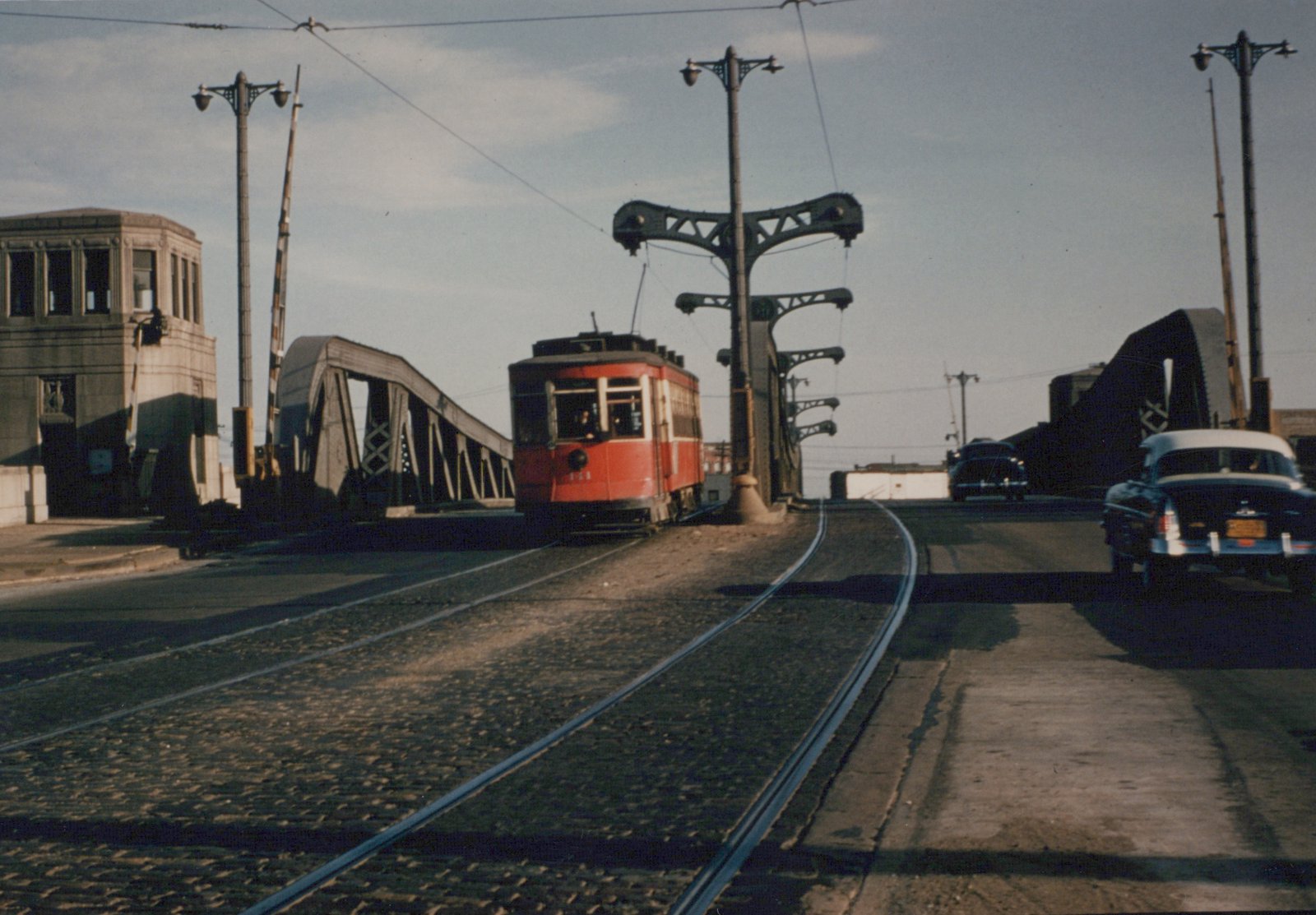 A red and white Chicago Surface Lines streetcar numbered 141 is positioned on a bascule bridge with vintage cars and a control tower nearby under a clear sky.