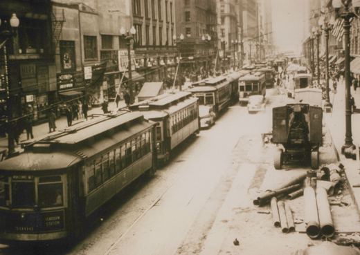 A black and white street scene showing a Chicago Surface Lines streetcar numbered 3006 on the front, pulling a second car down a busy city street lined with buildings and pedestrians.