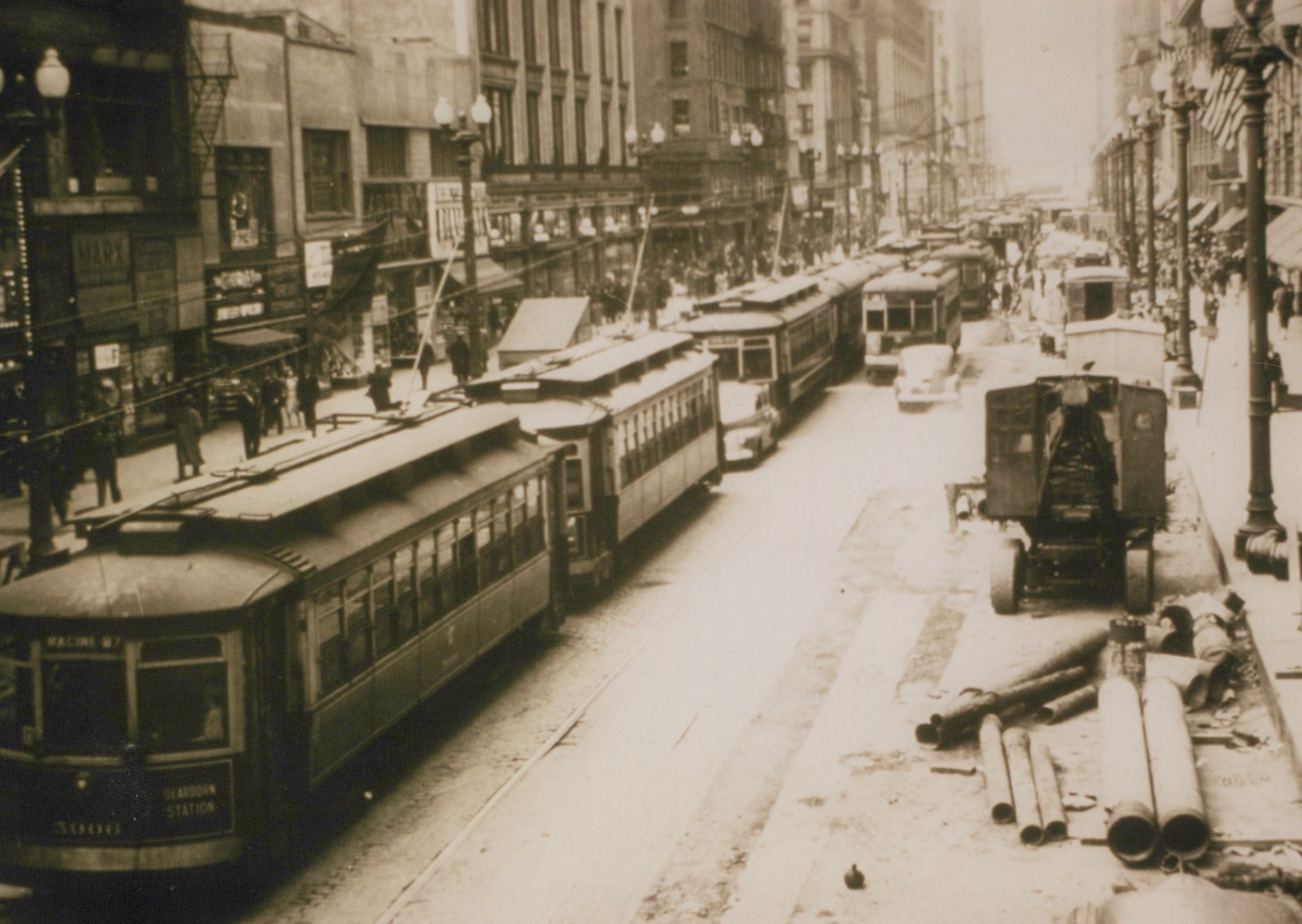 A black and white street scene showing a Chicago Surface Lines streetcar numbered 3006 on the front, pulling a second car down a busy city street lined with buildings and pedestrians.