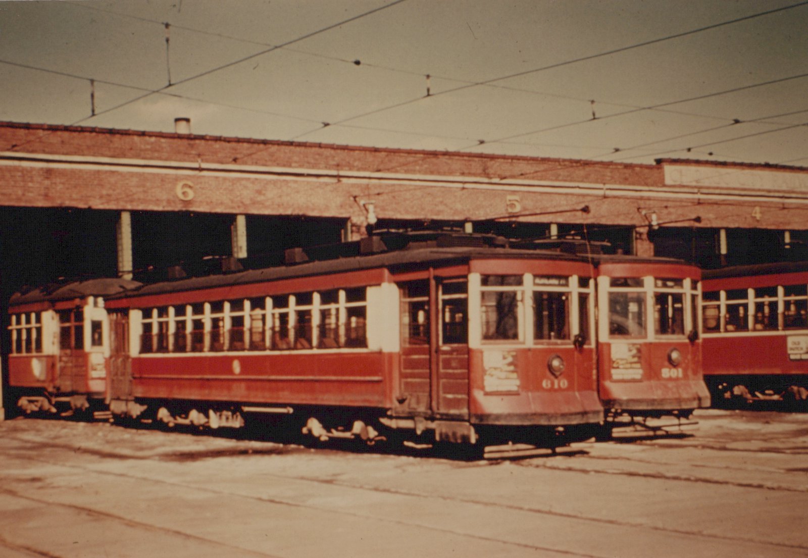 Two red and cream streetcars with numbers 610 and 501 are parked in a brick carbarn; the front of car 610 shows a destination sign reading 'ASHLAND AV'.