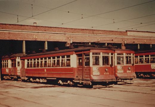 Two red and cream streetcars with numbers 610 and 501 are parked in a brick carbarn; the front of car 610 shows a destination sign reading 'ASHLAND AV'.