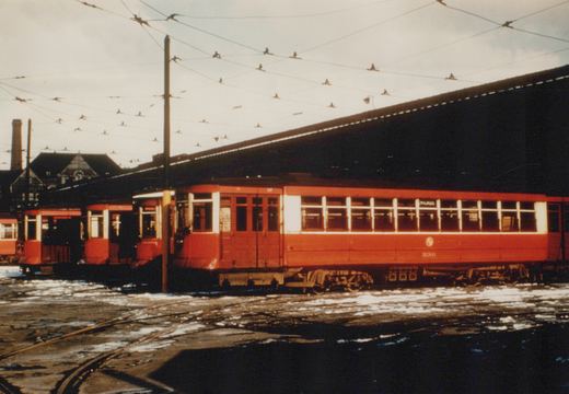 Three red and white interurban cars from the Chicago North Shore and Milwaukee line are parked side-by-side in a snowy yard, with complex overhead wiring above them.