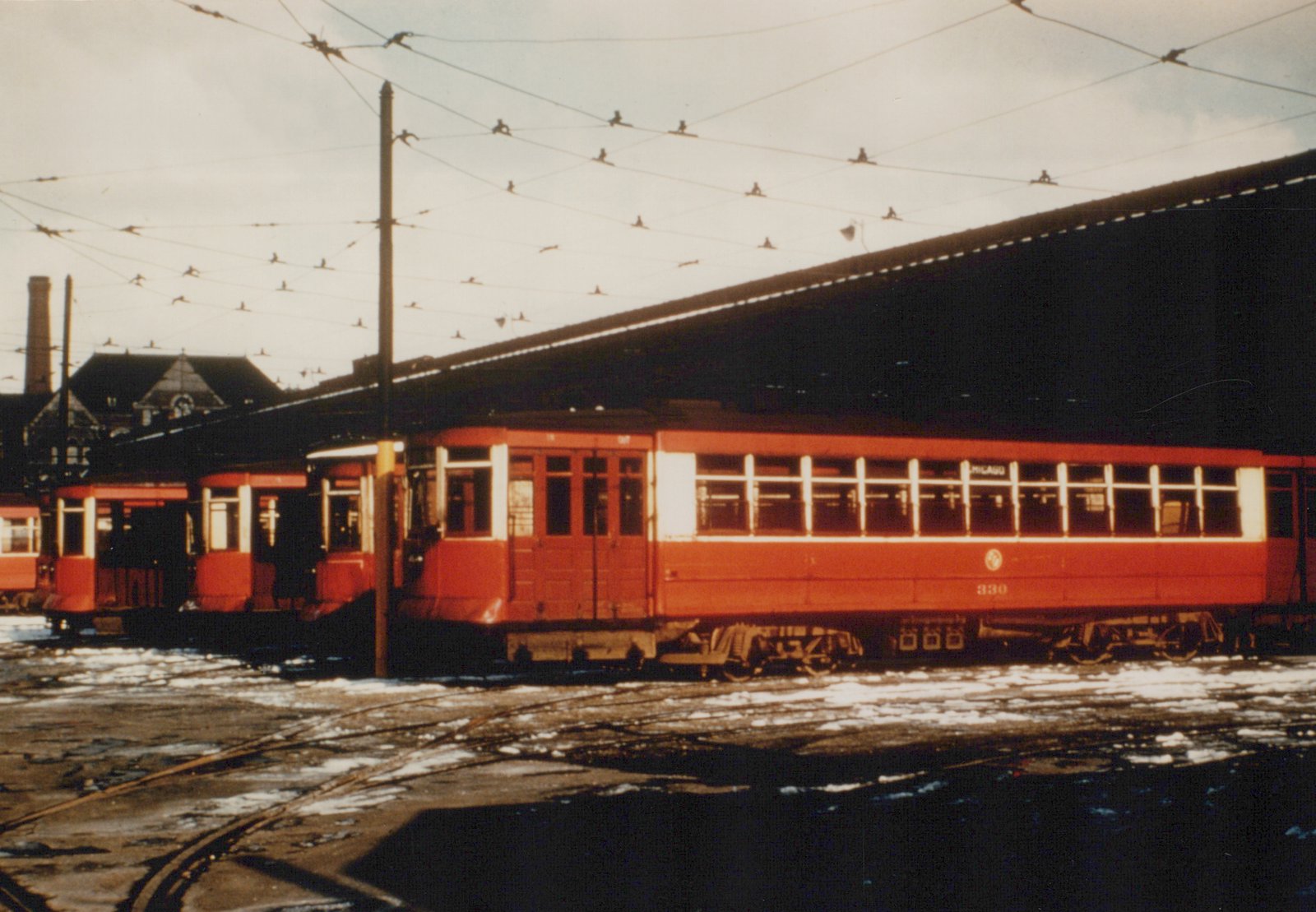 Three red and white interurban cars from the Chicago North Shore and Milwaukee line are parked side-by-side in a snowy yard, with complex overhead wiring above them.