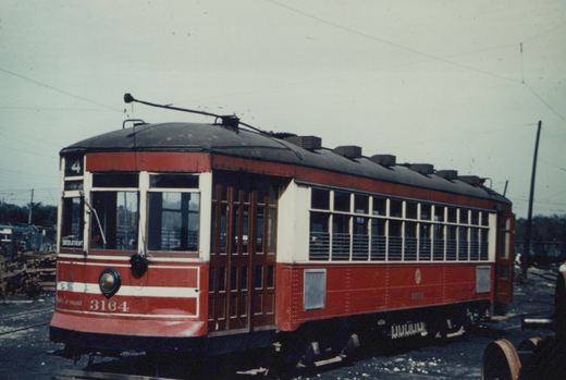 A red and cream vintage streetcar numbered 3164, identified as a Chicago Surface Lines Master Unit, is parked in a rail yard with overhead wires visible and a route number 4 sign on the front.