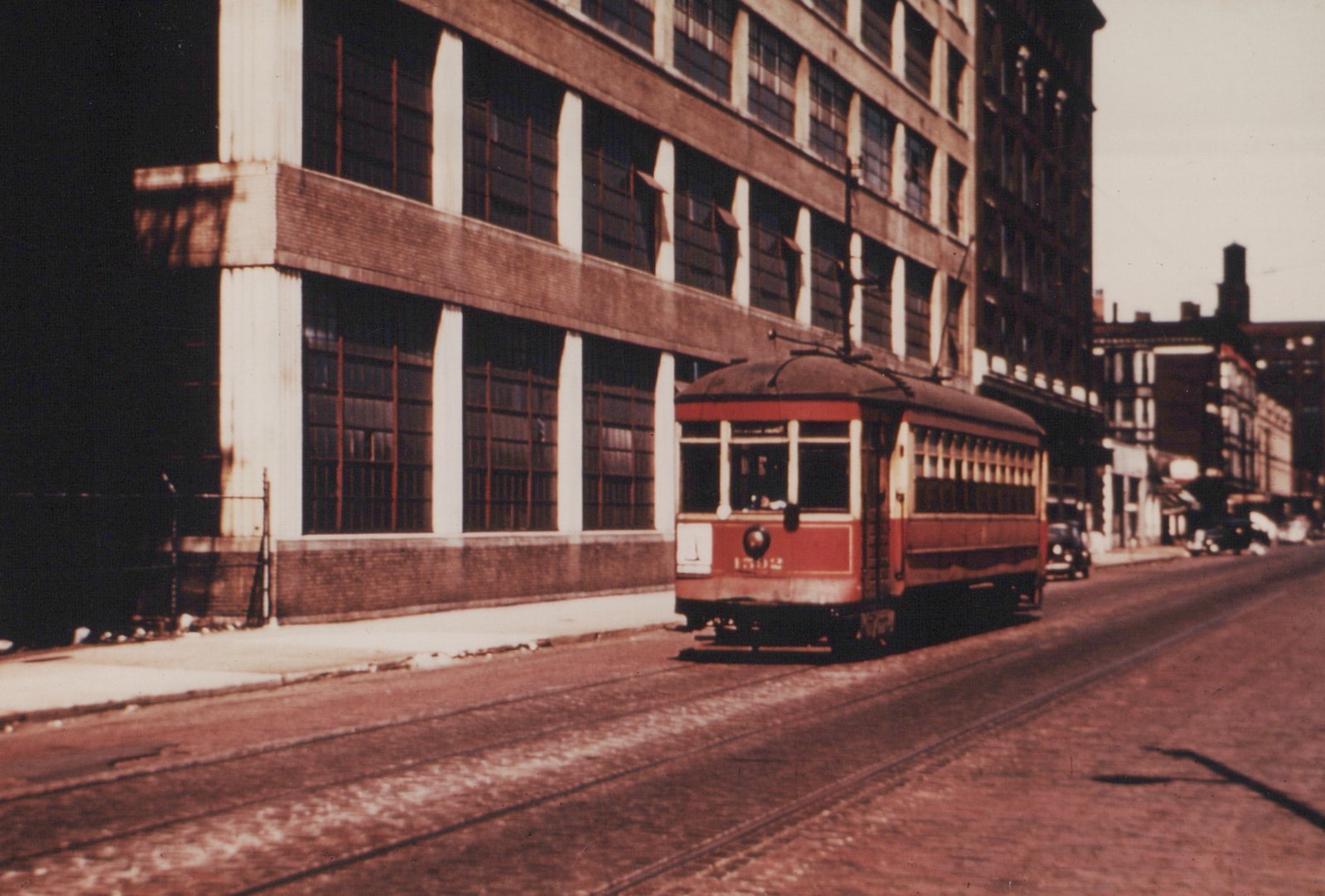 A red and cream streetcar from the Chicago Surface Lines, numbered 1592, is shown on a city street with a large industrial building and an automobile in the background.