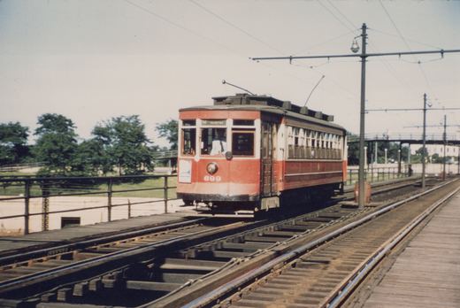 A red and cream interurban car numbered 699 with a destination sign reading 16 AUSTIN, traveling on an elevated wooden trestle with overhead wires.