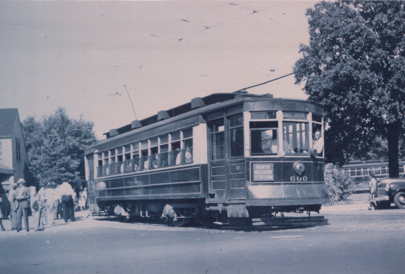 A vintage black-and-white photo of a Chicago Surface Lines streetcar, number 600, with passengers inside, a conductor in the front, and people on the street under a network of overhead wires.