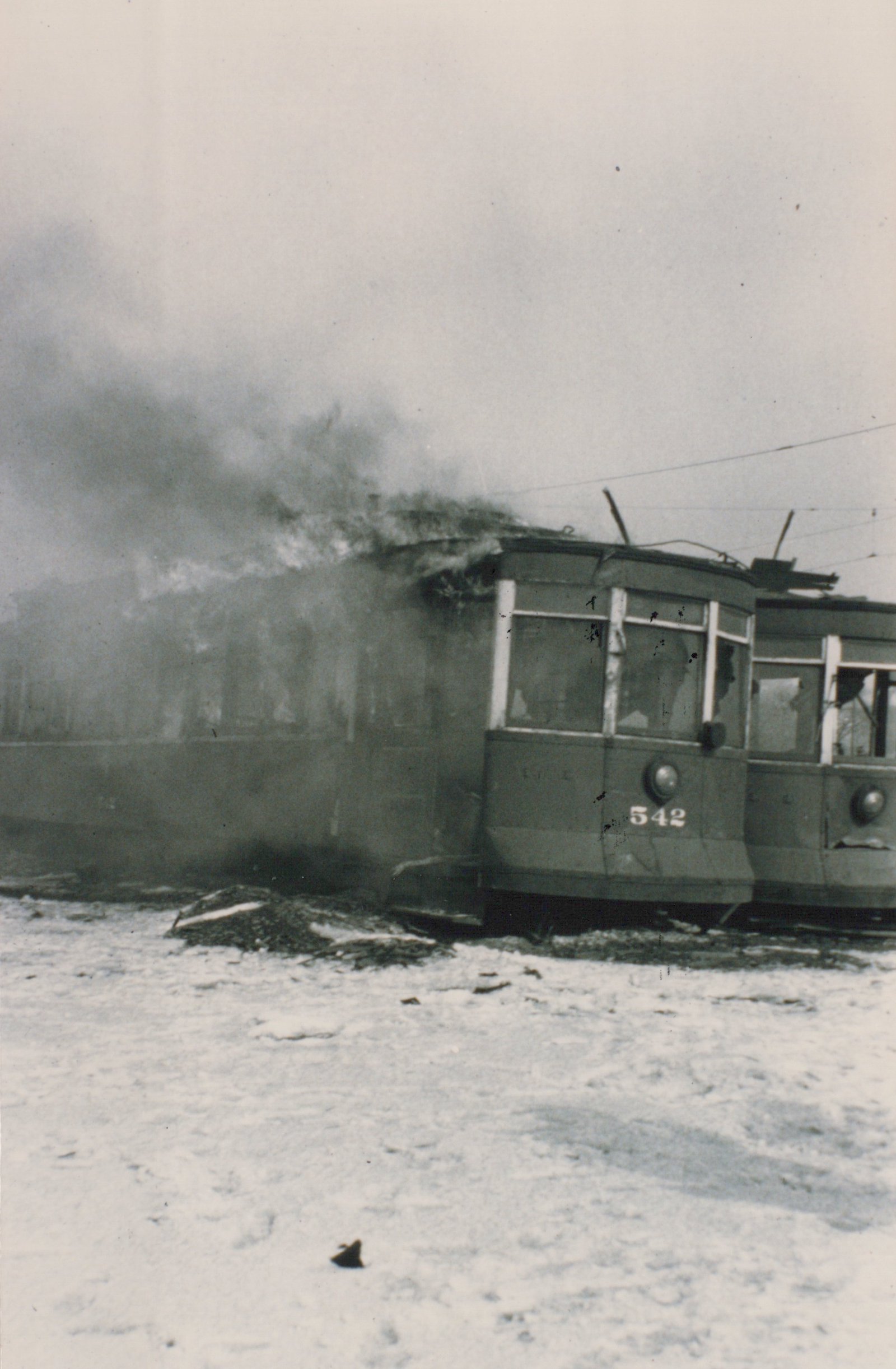 A vintage black and white photo shows a streetcar on fire in the snow, with the number 542 visible on its front.